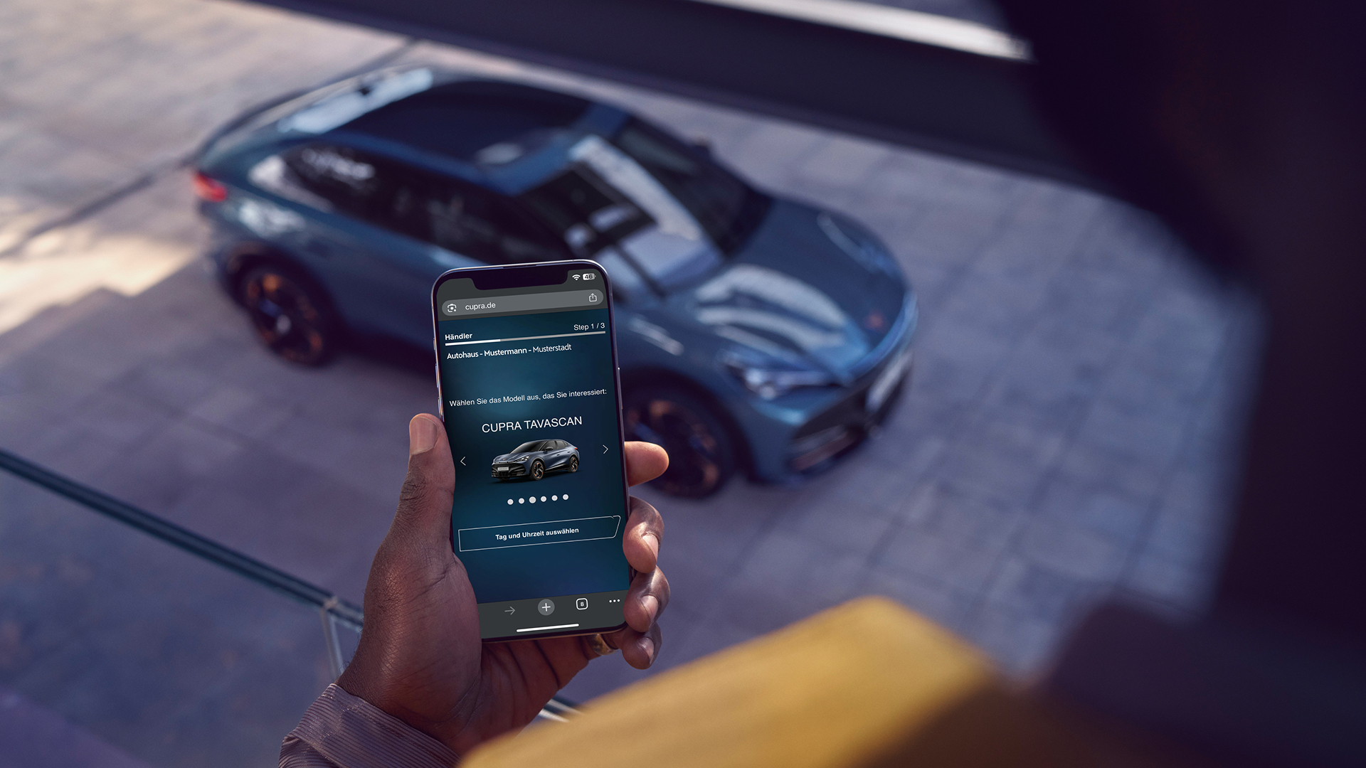 CUPRA Tavascan von schräg oben mit Person im Vordergrund, die eine Probefahrtbuchung am Smartphone tätigt